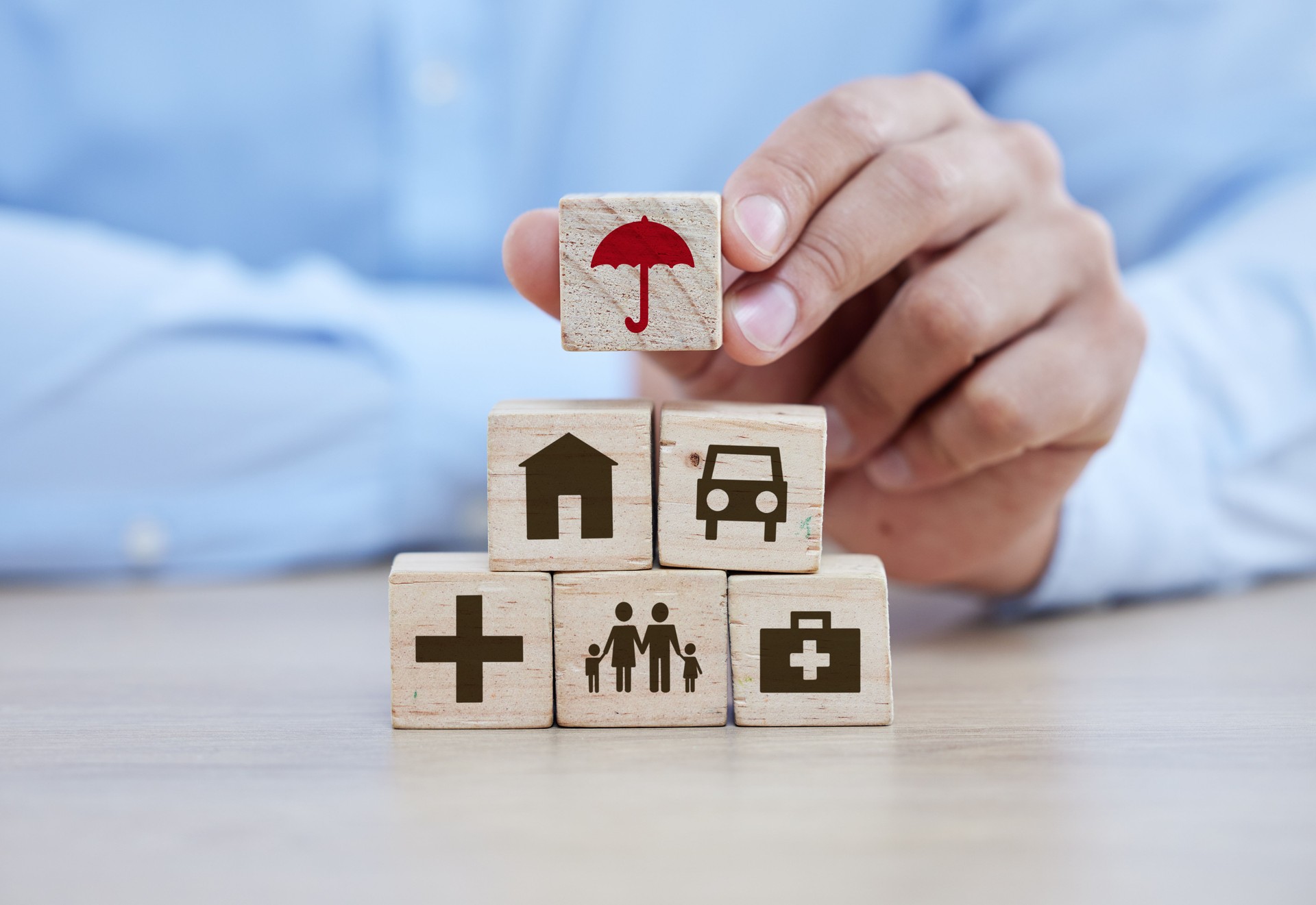 Salud, seguro de vida y bloques de construcción con manos del hombre para la seguridad, la medicina y la planificación. Futuro, inversión y jubilación con torre cubo de madera sobre mesa para ahorro, propiedad y medicina